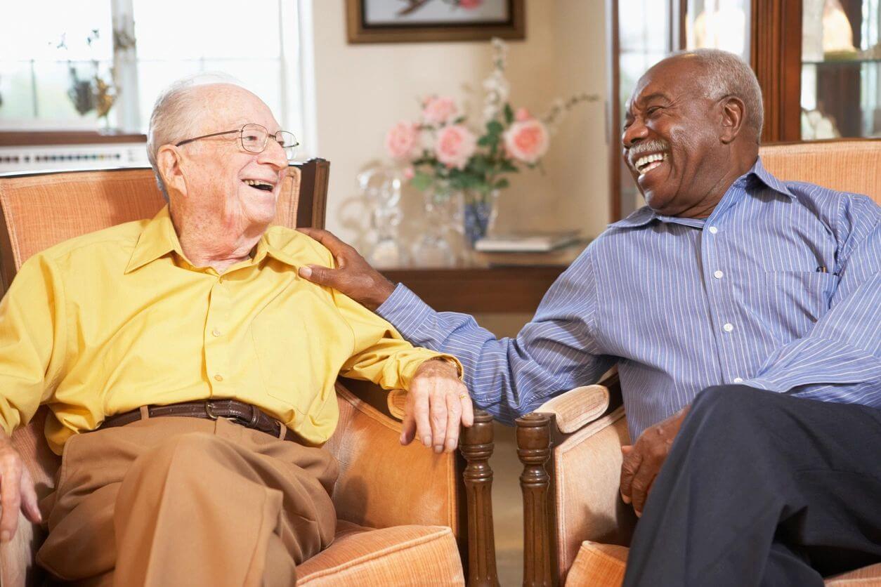 Two elderly men sitting on sofa talking and laughing